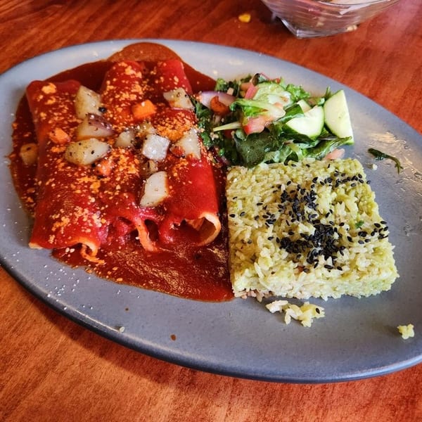 Three enchiladas covered in red sauce with rice and a side salad on a gray plate.