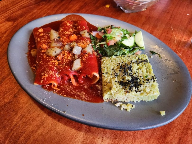 Three enchiladas covered in red sauce with rice and a side salad on a gray plate.