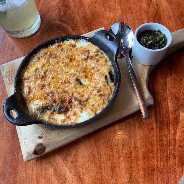 Baked cheese dish in a cast iron skillet with a side of sauce and a cocktail.