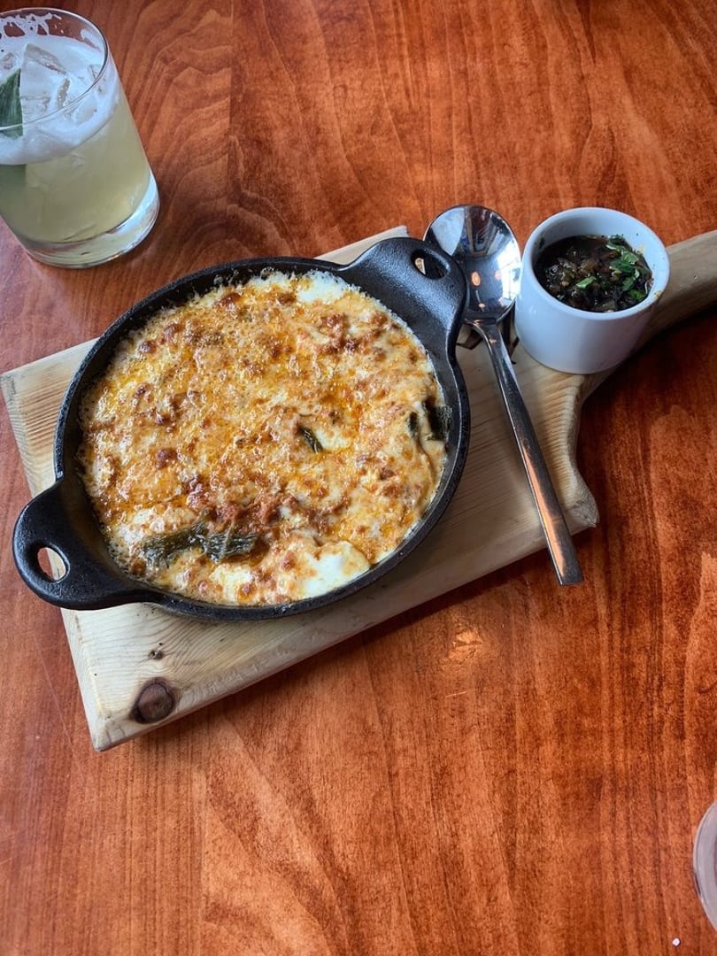 Baked cheese dish in a cast iron skillet with a side of sauce and a cocktail.