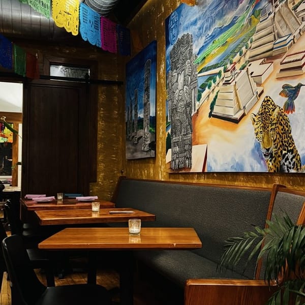Restaurant interior with colorful papel picado, Mayan-inspired murals, wooden tables, and a long booth.