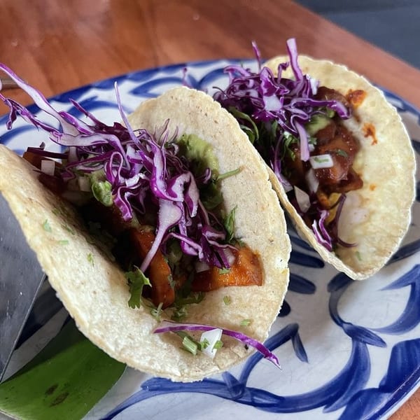 Two tacos with red cabbage, meat, and guacamole on a blue and white patterned plate.