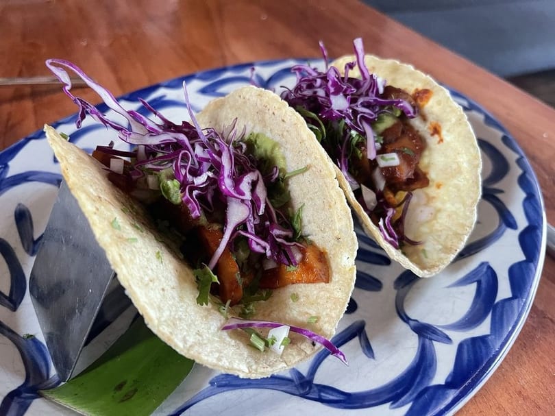 Two tacos with red cabbage, meat, and guacamole on a blue and white patterned plate.