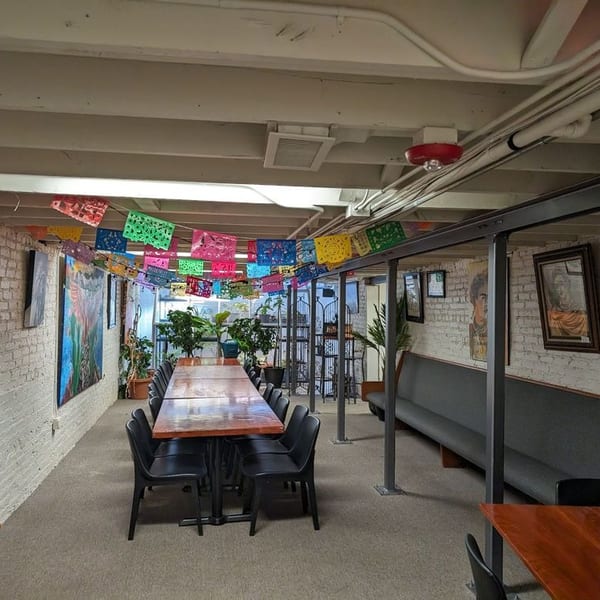 Long dining tables and benches in a restaurant basement decorated with colorful papel picado.
