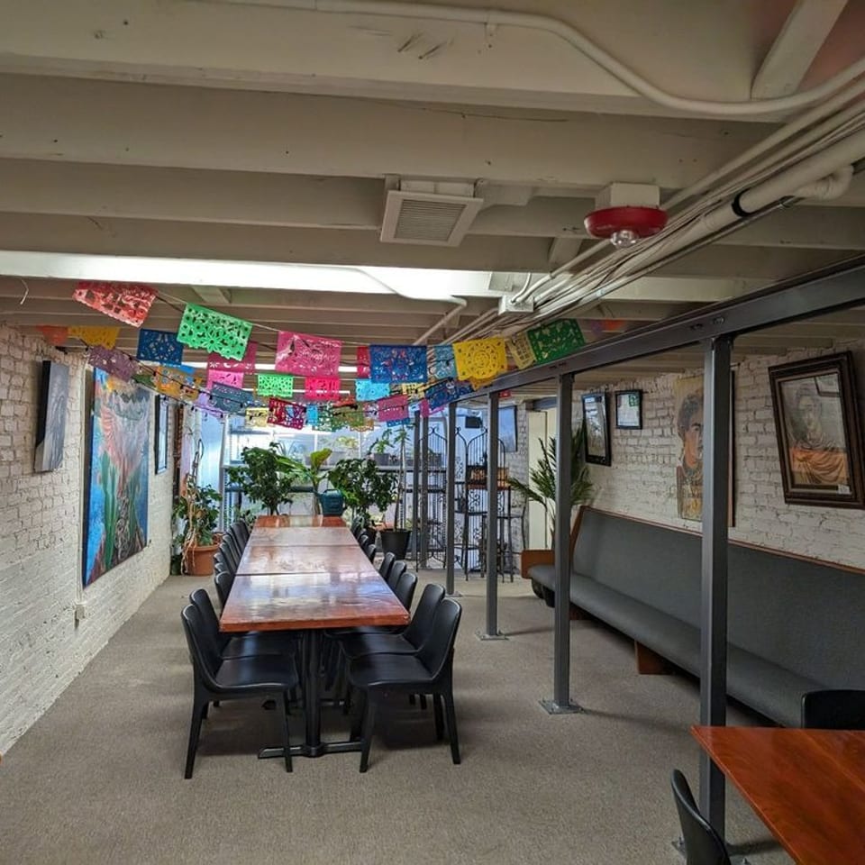 Long dining tables and benches in a restaurant basement decorated with colorful papel picado.