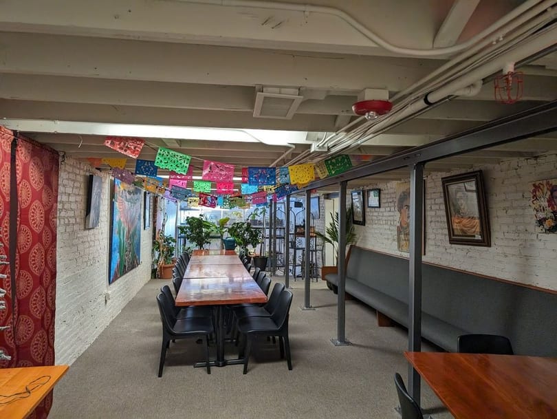 Long dining tables and benches in a restaurant basement decorated with colorful papel picado.