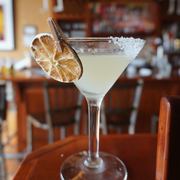 Salt-rimmed margarita with a dried lime slice on a wooden table in a restaurant.
