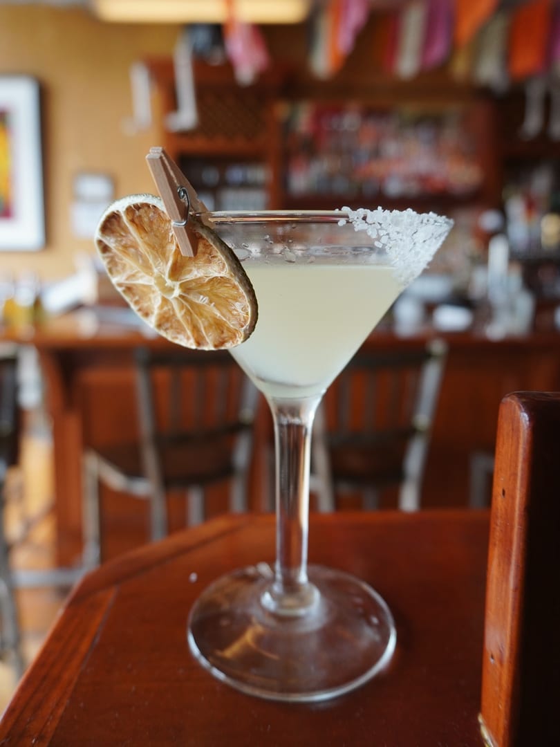Salt-rimmed margarita with a dried lime slice on a wooden table in a restaurant.