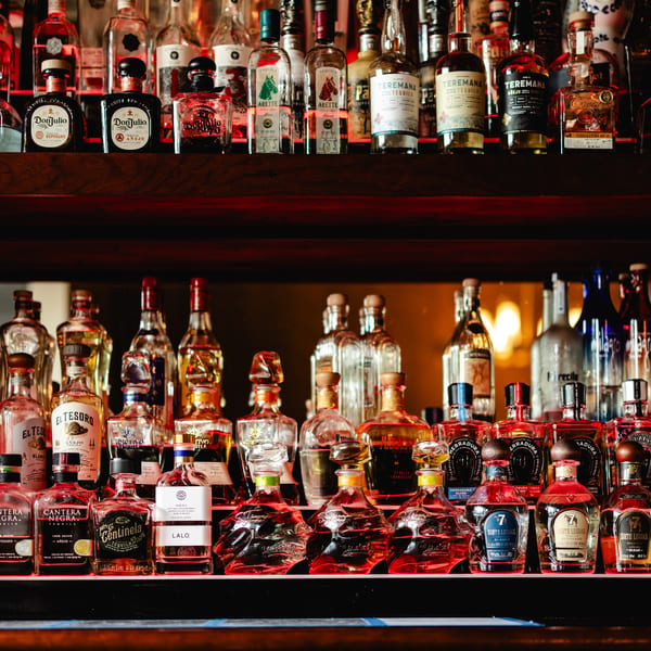 A large collection of tequila bottles, including Don Julio and Teremana, displayed on shelves.